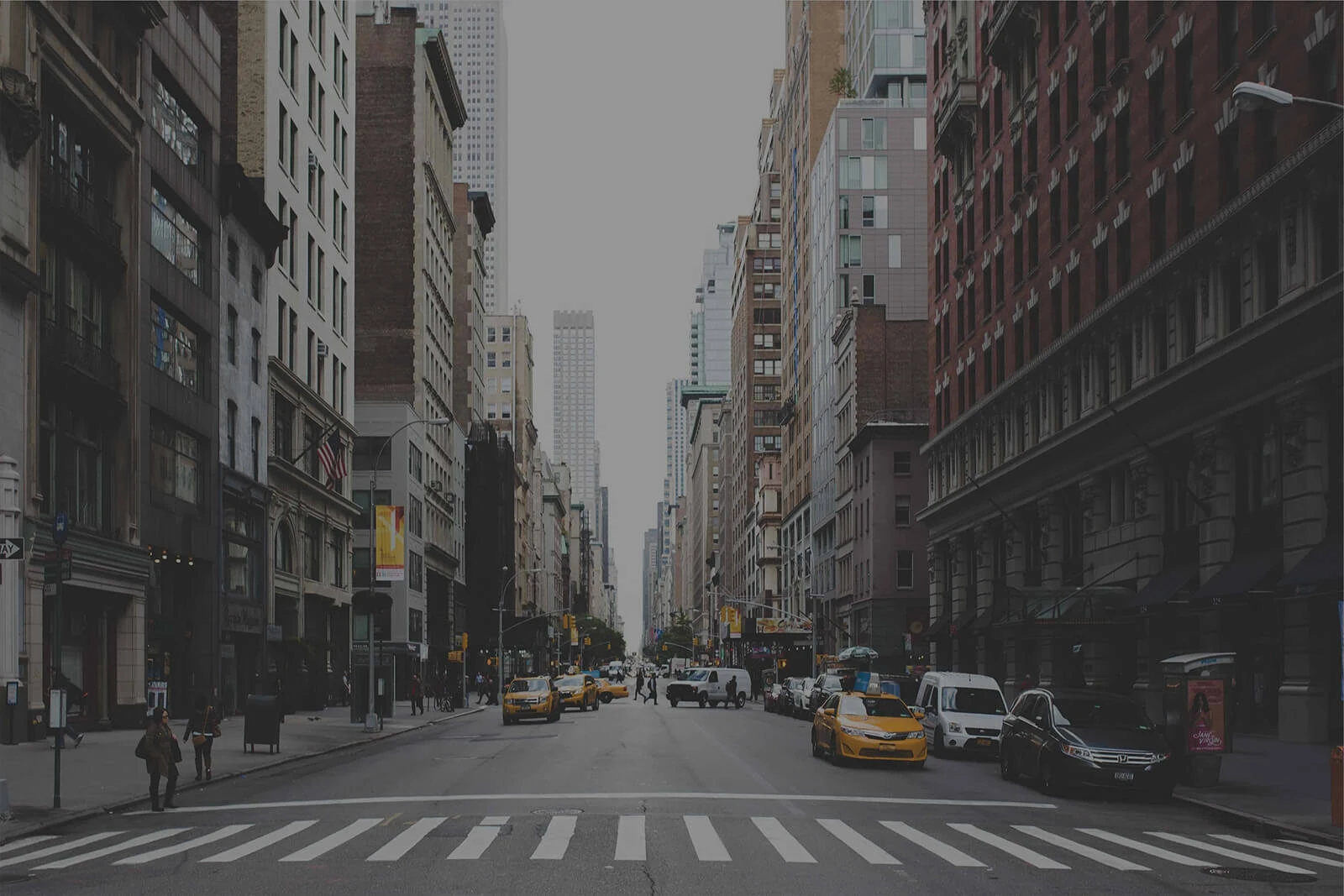 city street with tall building on either side, cabs and people on the street and side walks.