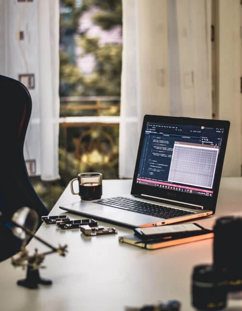 Laptop, coffee, notebook and phone on a desk.