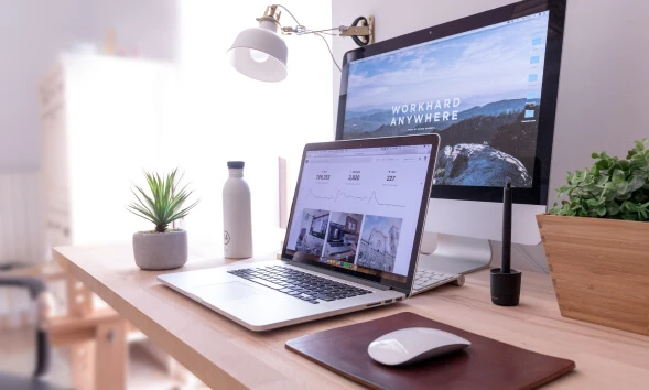 desk top and lap top computers on a desk showing work from home set up.