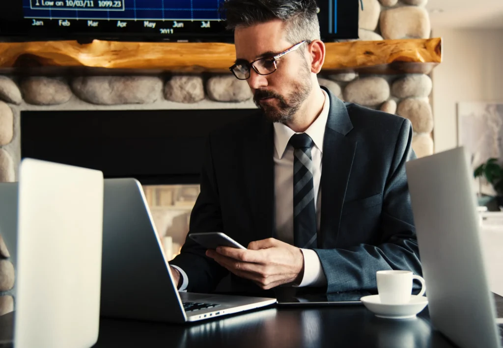 Attorney in dark suit, looking at a laptop while holding a smart phone.